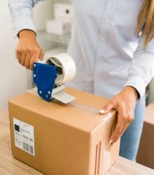 Business owner ready to ship her customers' orders. Close up of female hands putting tape on a big package with products