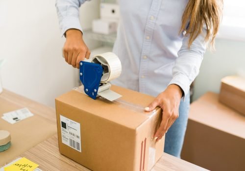 Business owner ready to ship her customers' orders. Close up of female hands putting tape on a big package with products